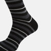 View 4 of product The Turnbull & Asser Chocolate Melange Striped Merino Wool Long Sock features black, dark gray, and light gray horizontal stripes and is displayed individually on a white background.