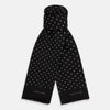 View 1 of product The Black and White Spotted Silk Scarf by Turnbull & Asser features a spotted design, neatly folded at the top and spread out at the bottom, with the brand's name printed in white near its fringed ends.