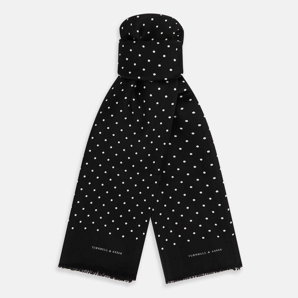 The Black and White Spotted Silk Scarf by Turnbull & Asser features a spotted design, neatly folded at the top and spread out at the bottom, with the brand's name printed in white near its fringed ends.