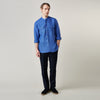 View 3 of product A man faces forward with a neutral expression, hands in his pockets, wearing the Turnbull & Asser Plain Indigo Linen Weekend Fit Shirt with a stand collar, styled with dark pants and black shoes against a plain light background.