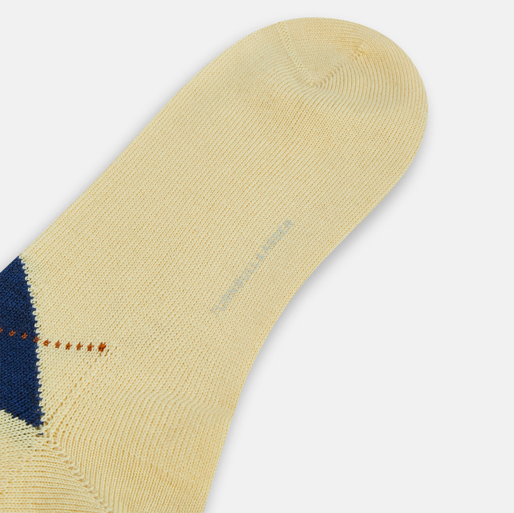 The Turnbull & Asser Vanilla Wool Check Mid-Length Sock is beige with blue, black, and white argyle diamonds on the side and solid beige toe, heel, and cuff. Displayed on a plain white background.