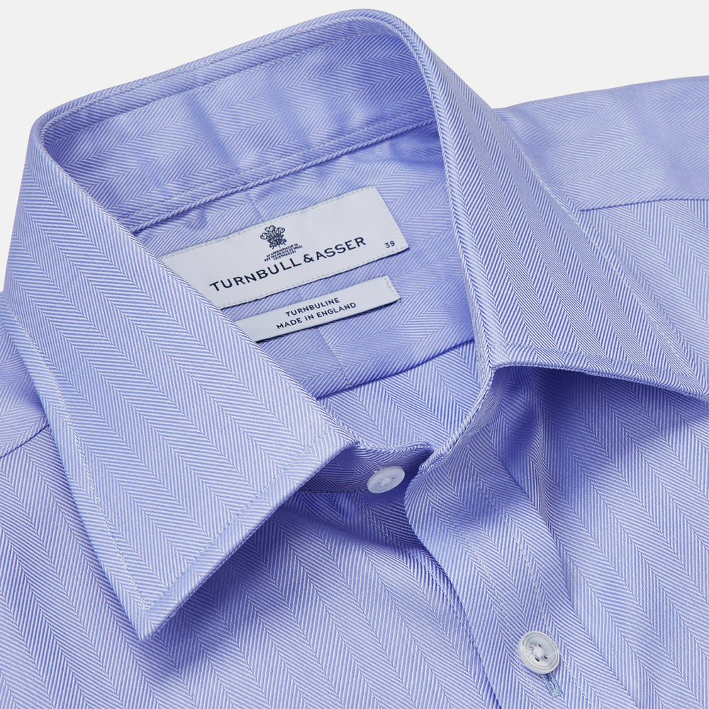 The Turnbull & Asser Blue Herringbone Regular Fit Shirt features a classic Kent collar, long sleeves, white buttons, and buttoned cuffs. Displayed on a white background, it's the perfect formal shirt for any occasion.