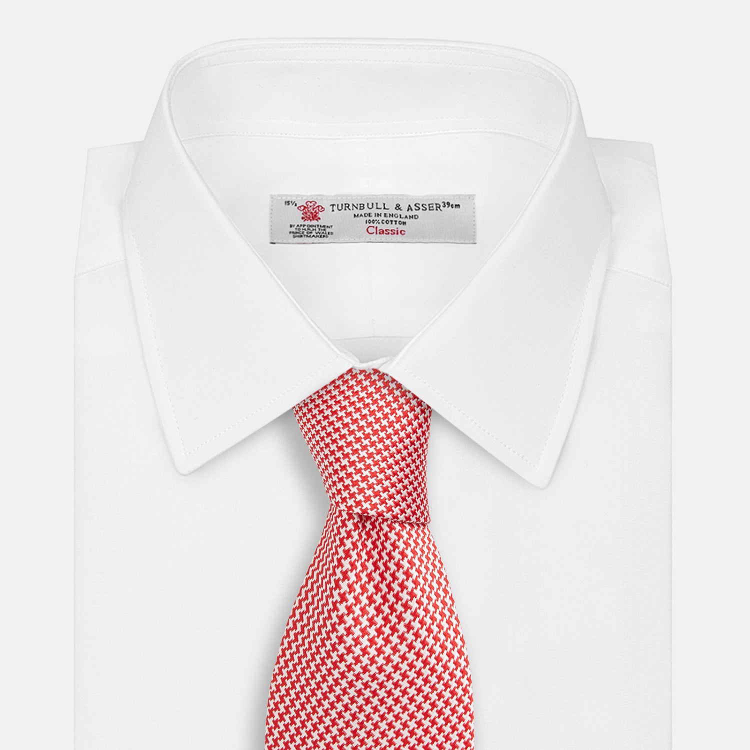 View 2 of product The Turnbull & Asser Red and White patterned silk tie, crafted from fine silk with a small geometric design, is elegantly rolled and displayed on a white background—a refined men’s accessory.