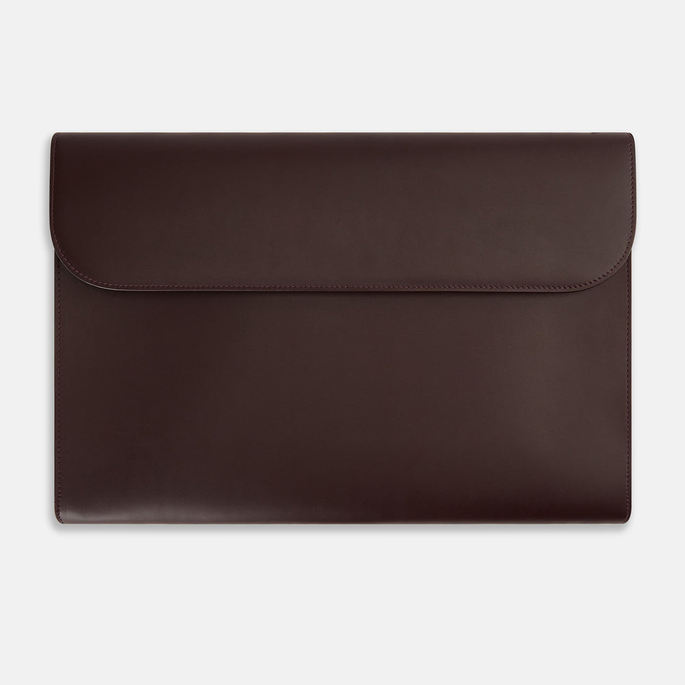 The Turnbull & Asser Burgundy Leather Snap-Fasten Pouch is a sleek, envelope-style laptop accessory with a smooth finish, curved flap, and elegant snap closure, ideal for business travel against a white background.