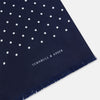 View 2 of product The Navy and White Spotted Silk Scarf by Turnbull & Asser features white polka dots, a fringed edge, and the brand's name printed near the bottom on both sides. It is neatly folded at the top.