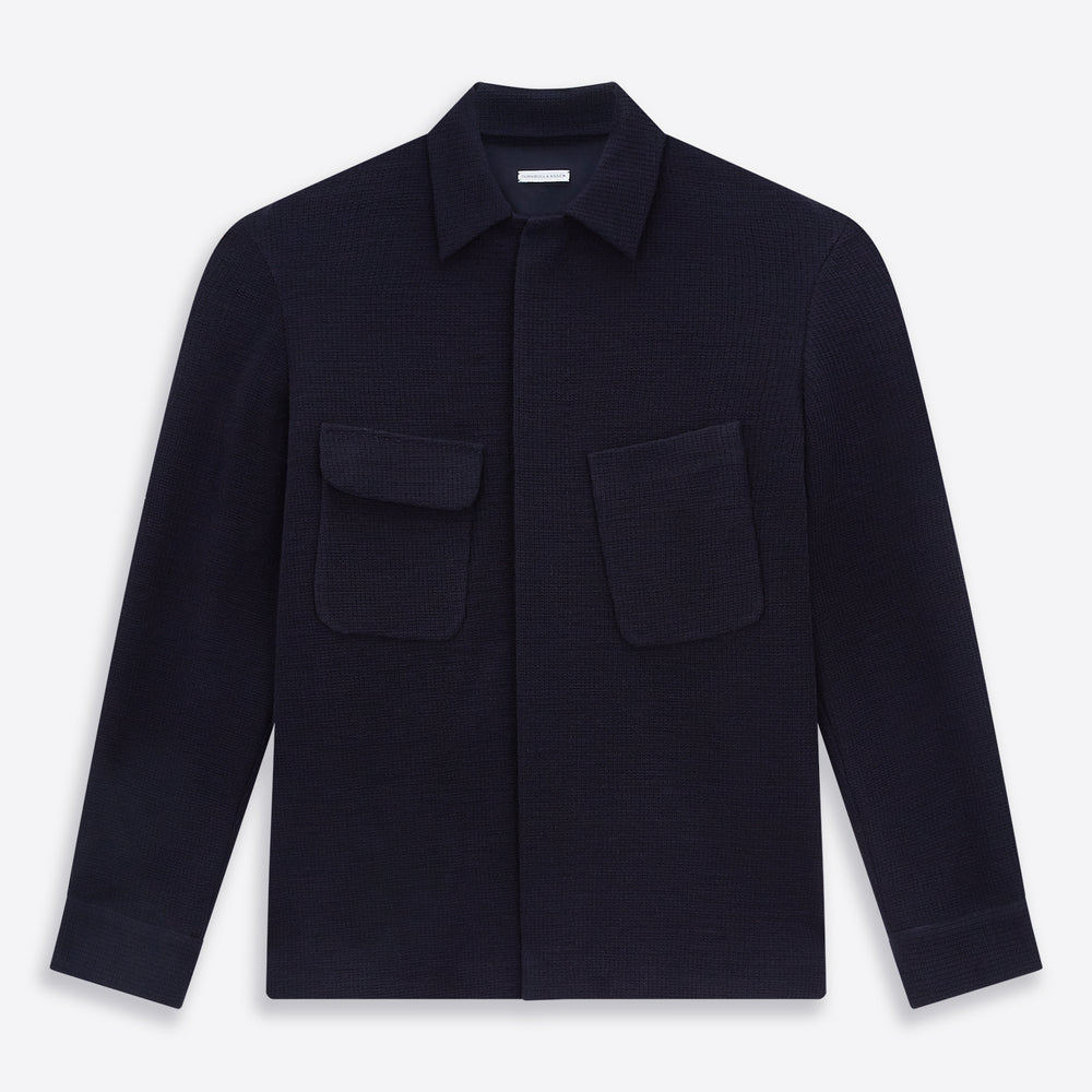 The Turnbull & Asser Navy Greenwich Knitted Overshirt, made from Italian wool with a collar, two front flap pockets, and a hidden button placket, is shown laid flat on a white background.