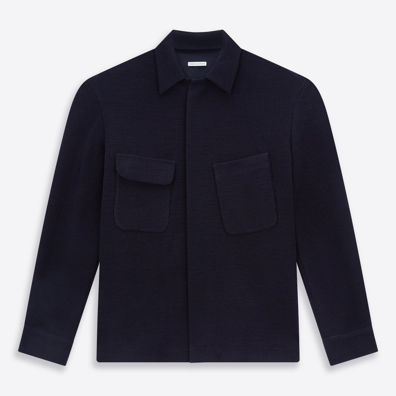 View 1 of product The Turnbull & Asser Navy Greenwich Knitted Overshirt, made from Italian wool with a collar, two front flap pockets, and a hidden button placket, is shown laid flat on a white background.