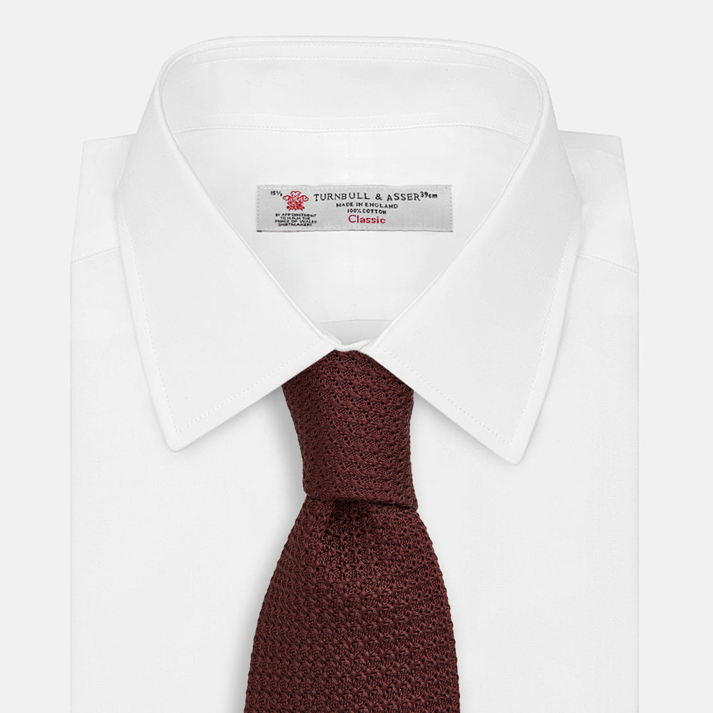 The Turnbull & Asser Dark Red Knitted Tie, featuring a textured finish, is shown rolled up against a white background—a stylish and versatile accessory ideal for the modern gentleman.
