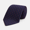 View 1 of product The Turnbull & Asser LACE ON TONE SPOT NAVY TULIP RED TIE is a classic men's accessory crafted from textured navy fabric with small red polka dots, neatly rolled with the pointed end facing forward.