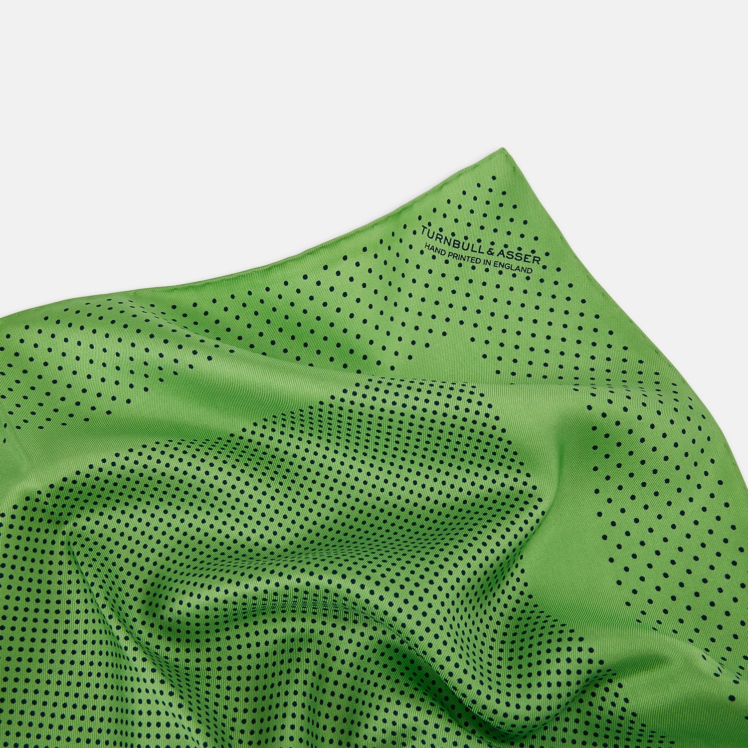 View 2 of product The Fern Green Dot Silk Pocket Square by Turnbull & Asser is crafted from pure silk, featuring a subtle black polka dot border with a denser dot pattern at the center and the brand name printed in the upper right corner.