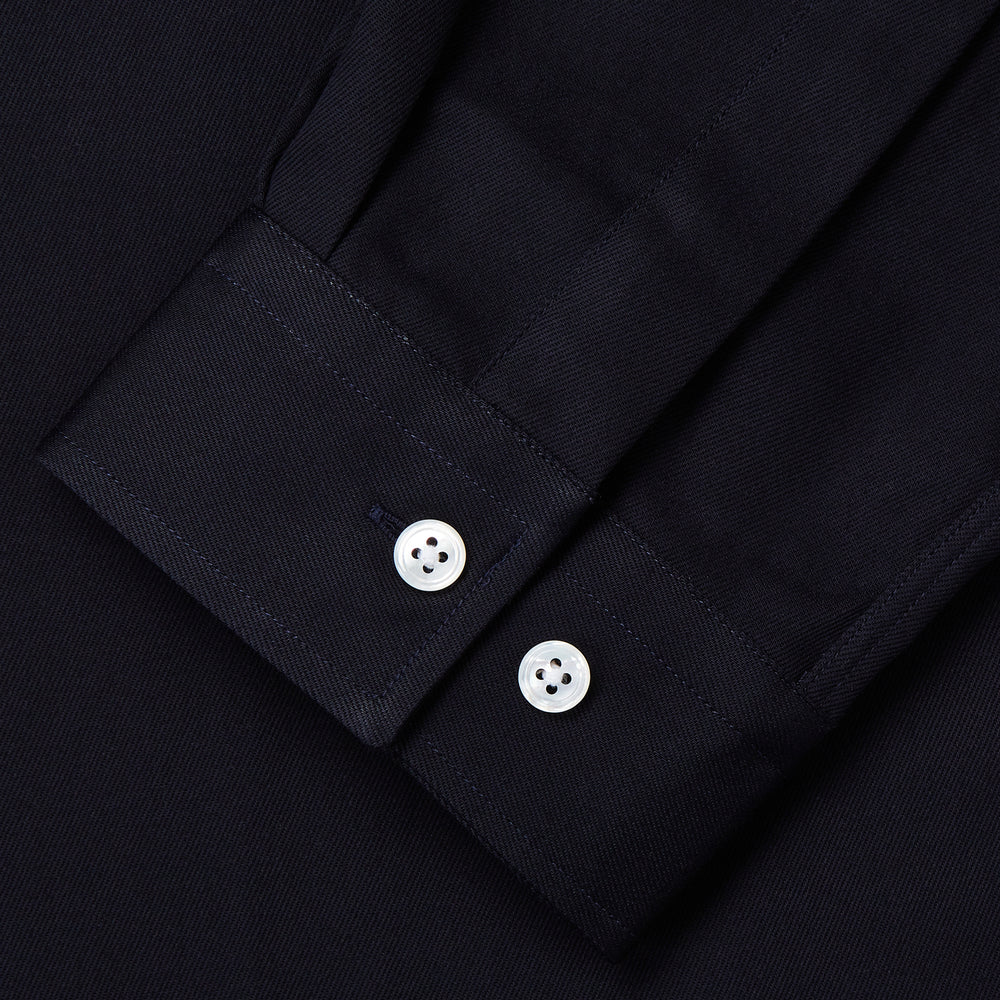 A Navy Cotton Holiday Fit Winnington Shirt by Turnbull & Asser, featuring long sleeves, a chest pocket, white buttons, and a revere collar, is laid flat on a white background.