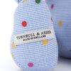 View 3 of product The Turnbuline Cotton Spot Teddy Bear by Turnbull & Asser is a blue gingham bear with colorful polka dots, black button eyes, a black nose, and a white leg label, shown sitting upright in profile facing left.