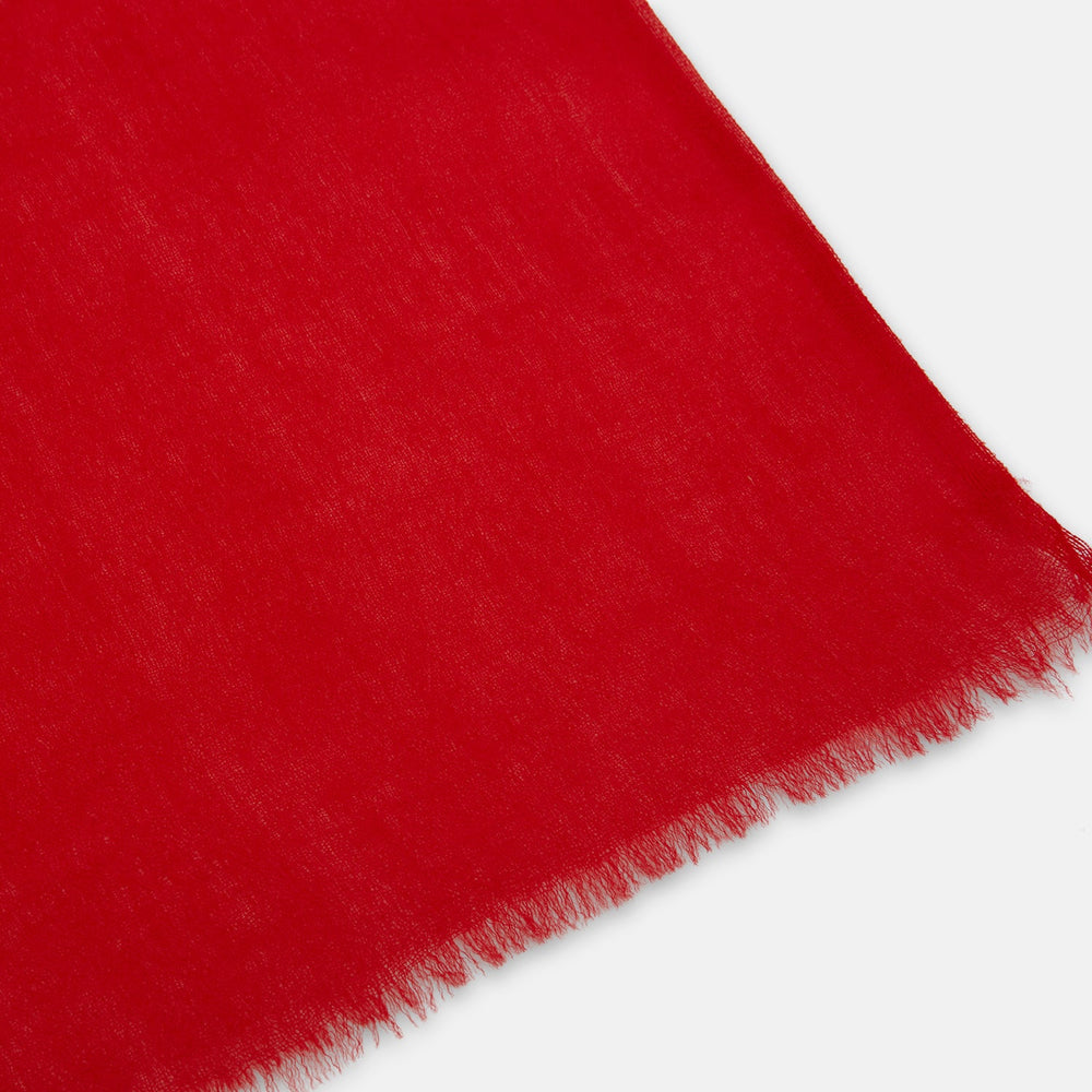 The Turnbull & Asser Red Cashmere Scarf features a soft texture, subtle frayed edges, and long ends. Loosely knotted against a plain light background, it’s an elegant accessory that adds a touch of style to any outfit.