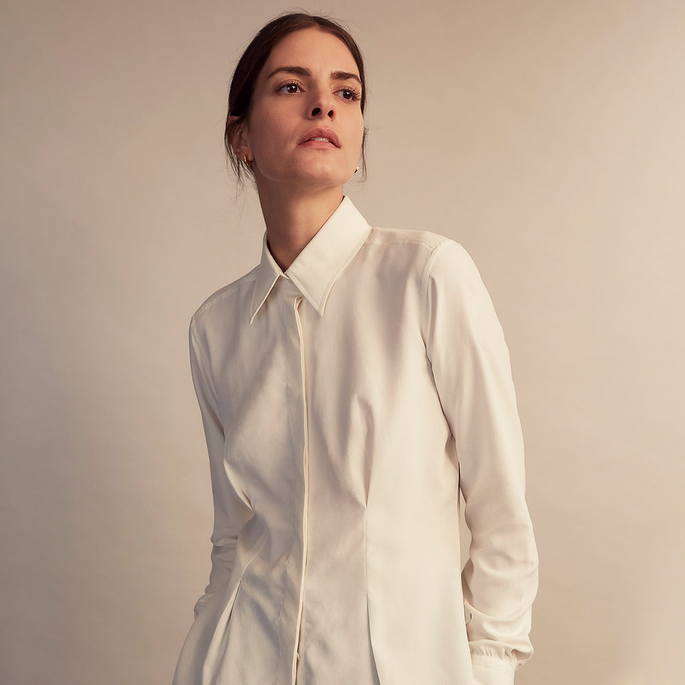 The Cream Silk Tailored Bianca Shirt by Turnbull & Asser features long sleeves, a pointed collar, and curved hem in soft-touch peace silk with a tailored fit. Shown laid flat on a white background.