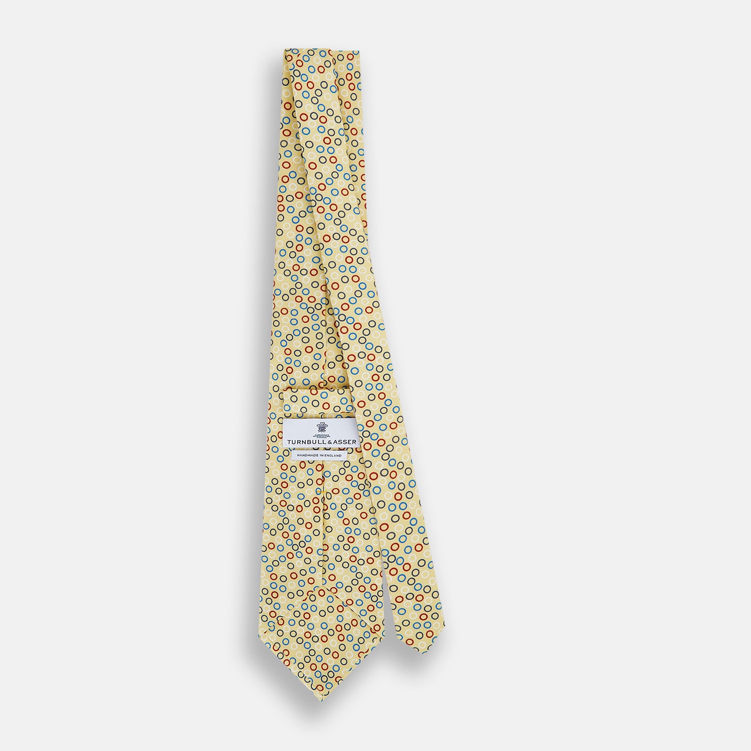 View 4 of product The Turnbull & Asser Multi-coloured Circle Yellow Silk Tie, crafted from fine English silk, features a vibrant pattern of multicoloured circles and is elegantly displayed rolled on a white background.