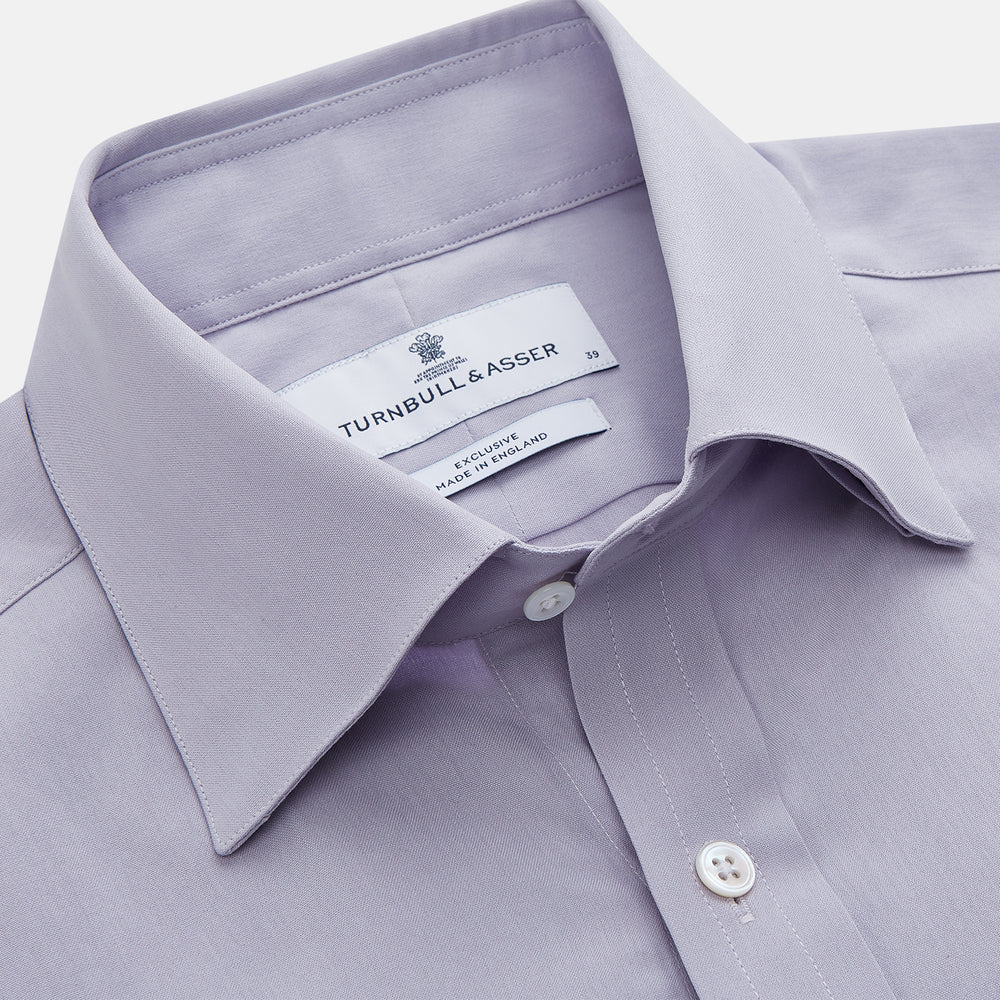 The Turnbull & Asser Lilac Silk Regular Fit Flaxton Shirt features long sleeves, a classic collar, white buttons, and a curved hem, shown laid flat on a white background.