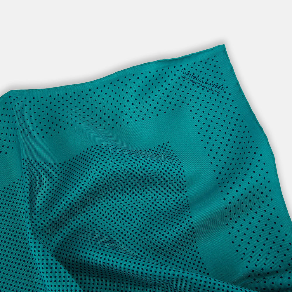 The Turnbull & Asser Petrol Green Dot Silk Pocket Square, made in England, features a border and small black polka dots, neatly folded to showcase both front and back sides.