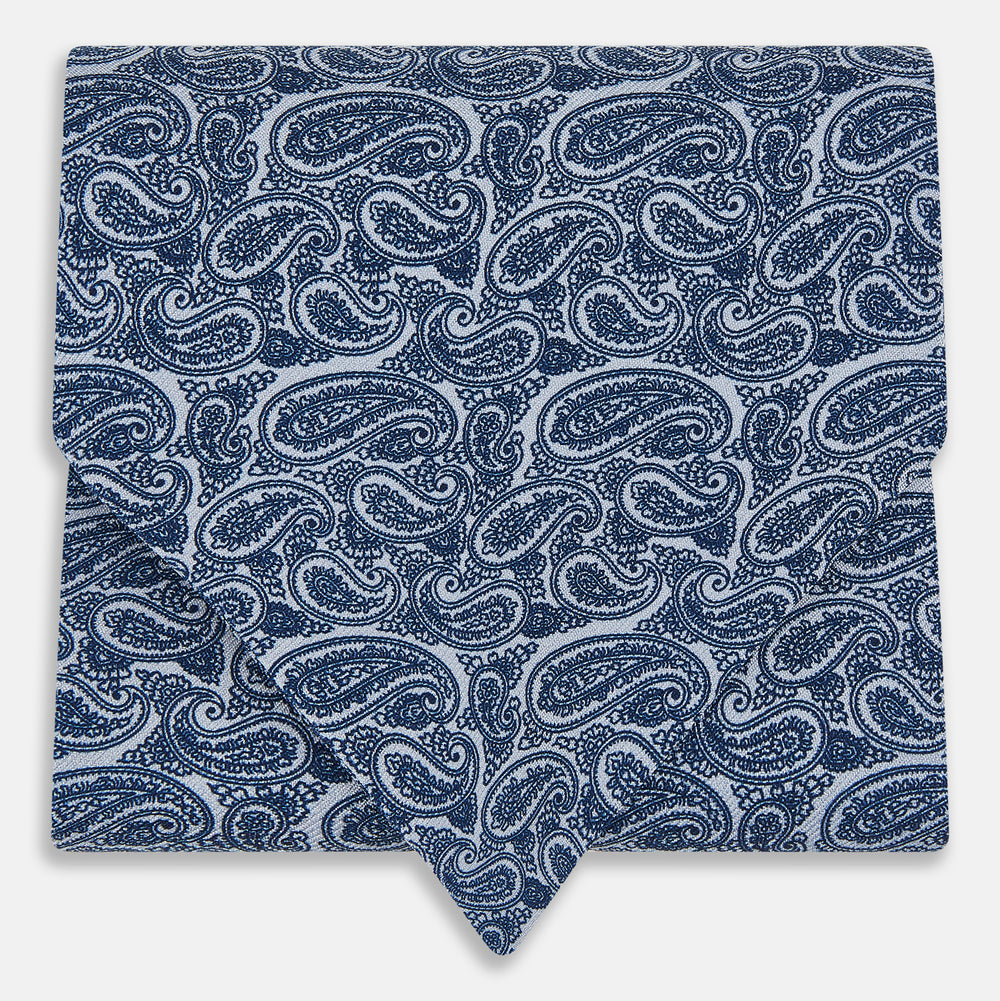 The Pale Blue Paisley Silk Cravat by Turnbull & Asser showcases intricate, swirling blue and white paisley designs on a light background, echoing the elegance of British style accessories.