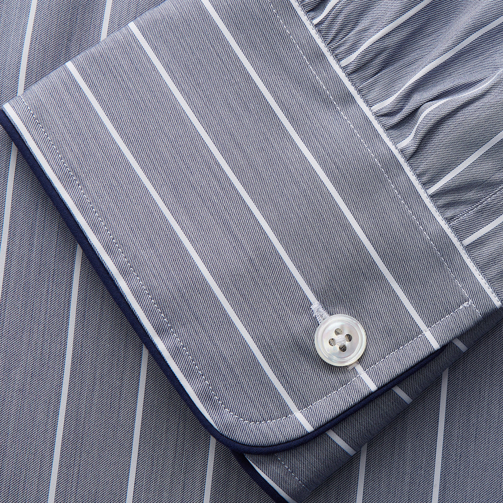 The Turnbull & Asser Pale Blue and White Pinstripe Cotton Blend Sussex Nightshirt pairs classic style with comfort, featuring long sleeves, a collar, front buttons, chest pocket, and curved hemline—perfect for luxury sleepwear.