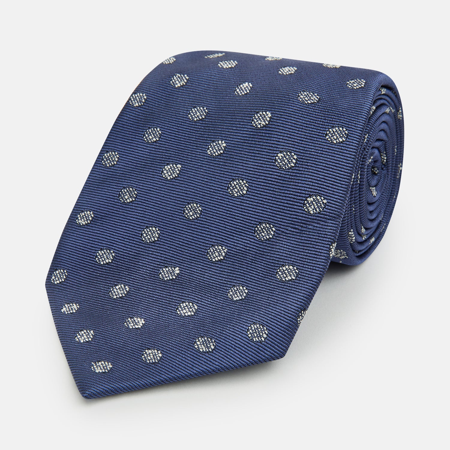 View 1 of product The Turnbull & Asser Navy Circle Silk Tie, made from pure silk with a navy base and small white dot pattern, is shown rolled up on a plain white background.
