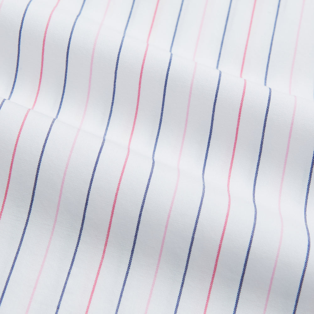 The Turnbull & Asser Pink and Blue Wide Pinstripe Mayfair Shirt features long sleeves, T&A collar, button-down front, and buttoned cuffs. It has bold pink and blue pinstripes on white and is laid flat on a white surface.