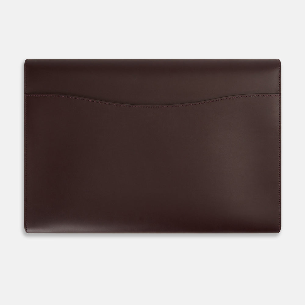 The Turnbull & Asser Burgundy Leather Snap-Fasten Pouch is a sleek, envelope-style laptop accessory with a smooth finish, curved flap, and elegant snap closure, ideal for business travel against a white background.