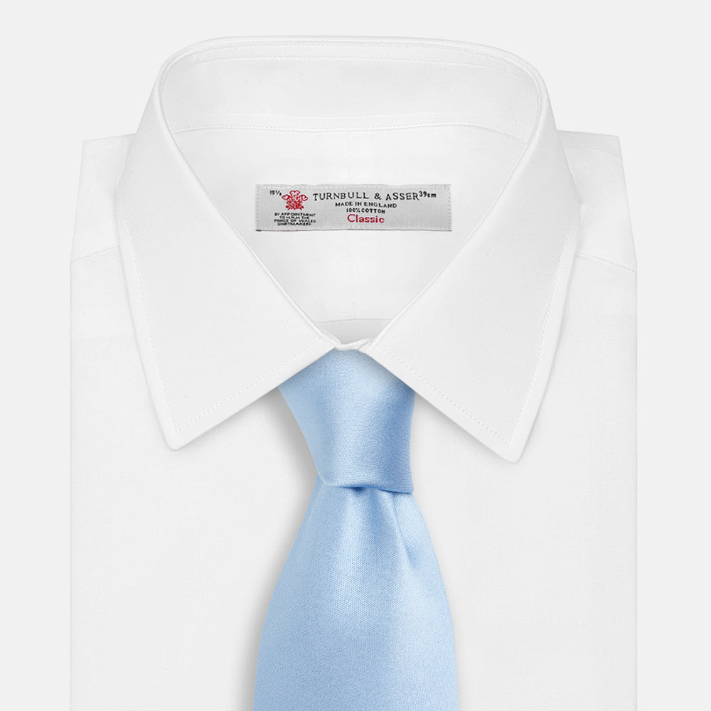 The Turnbull & Asser SATIN RIVER TIE, a neatly rolled light blue silk accessory with a smooth matte finish, is displayed against a plain white background.