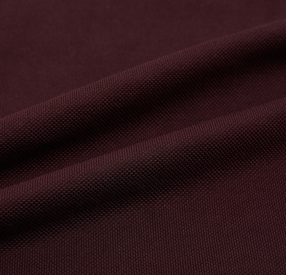 The Turnbull & Asser Burgundy Polo Shirt is crafted from soft cotton jersey with short sleeves, a classic collar, three front buttons, and a small buttoned chest pocket, shown flat on a white background.