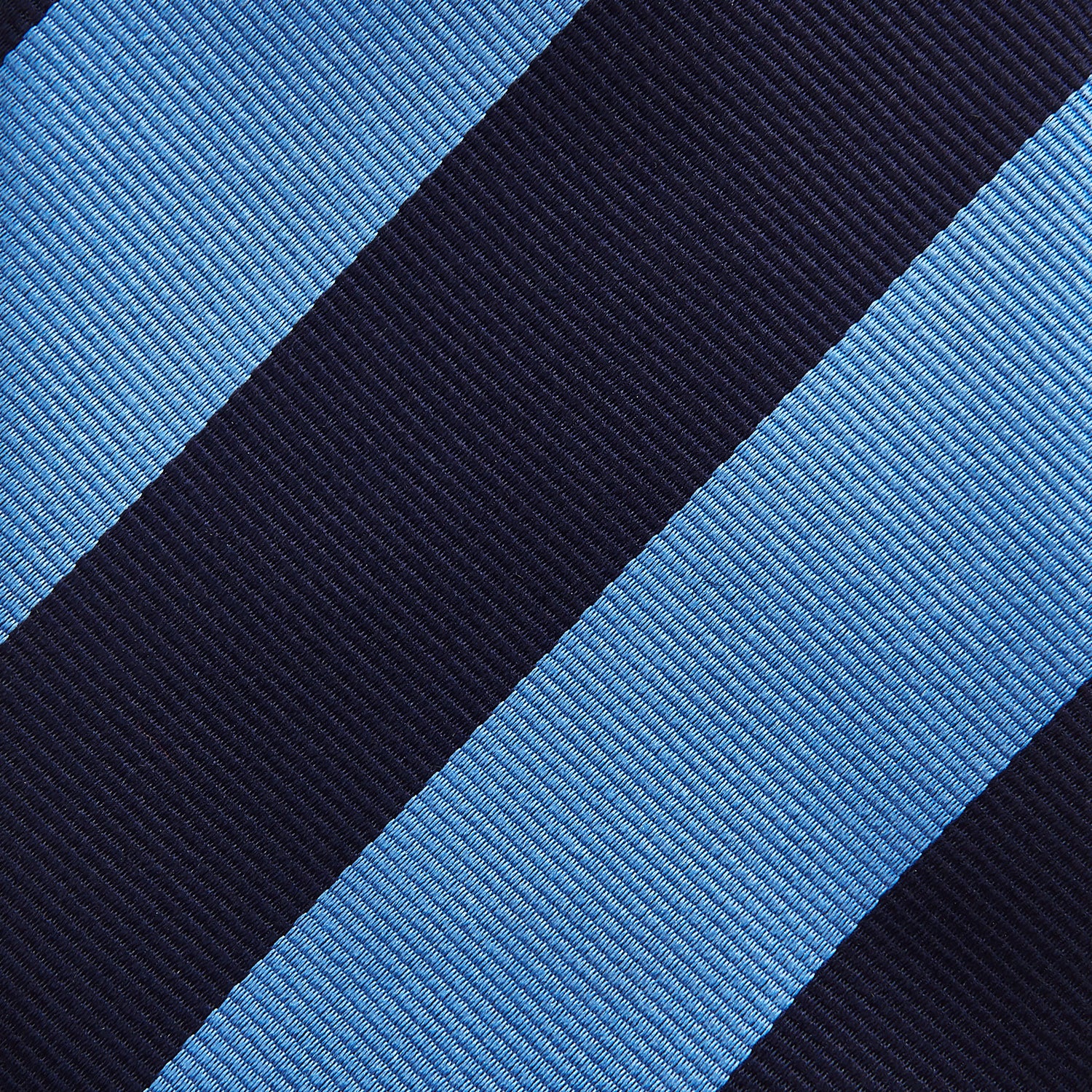 View 3 of product The BLOCK STRIPE NAVY RIVER TIE by Turnbull & Asser features bold navy and light blue diagonal stripes, rolled up neatly on a white background—a stylish essential for elevating any formal look.