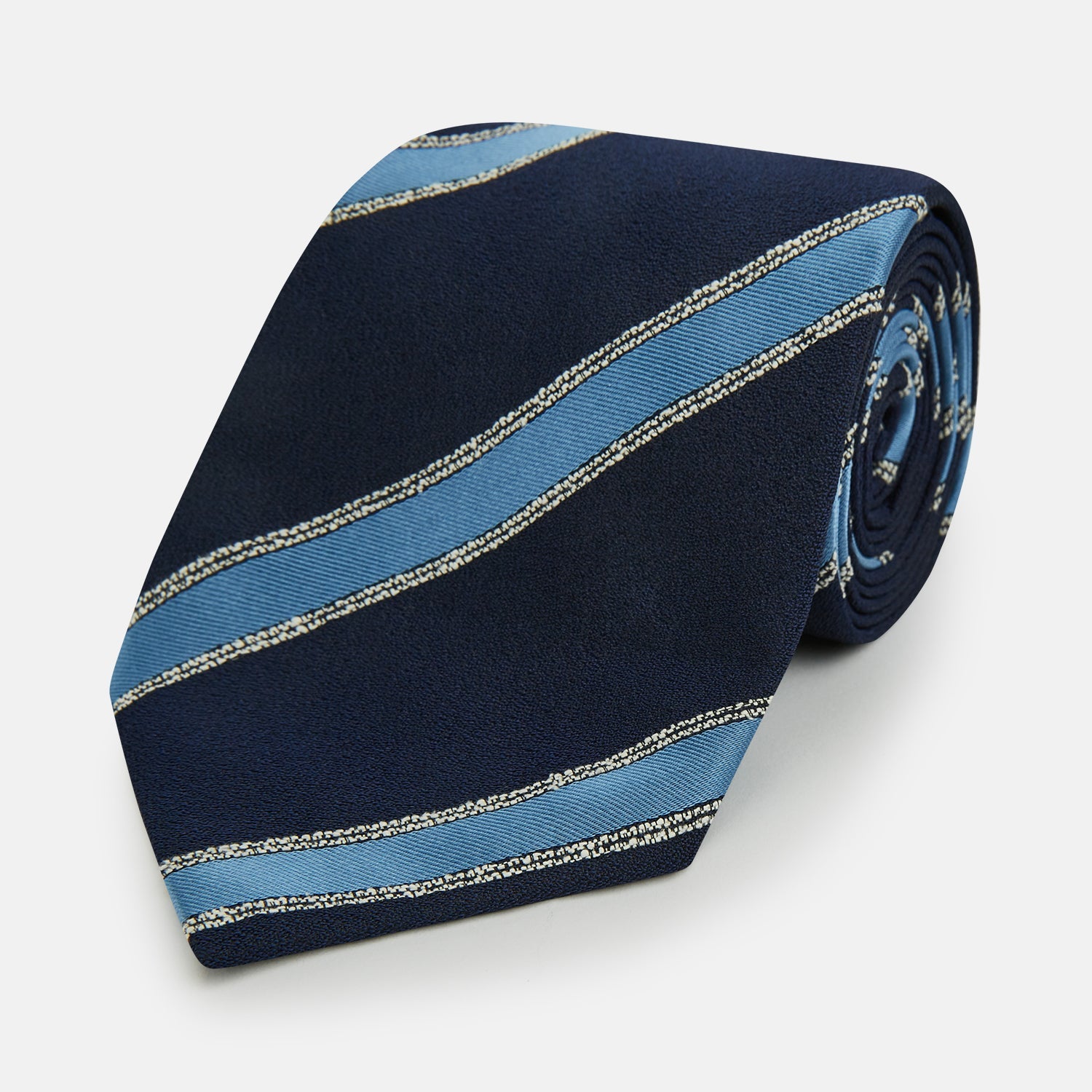 View 1 of product The Turnbull & Asser Navy Multi Stripe Silk Tie features diagonal light blue and silver stripes on an English silk navy base, rolled neatly against a white background.