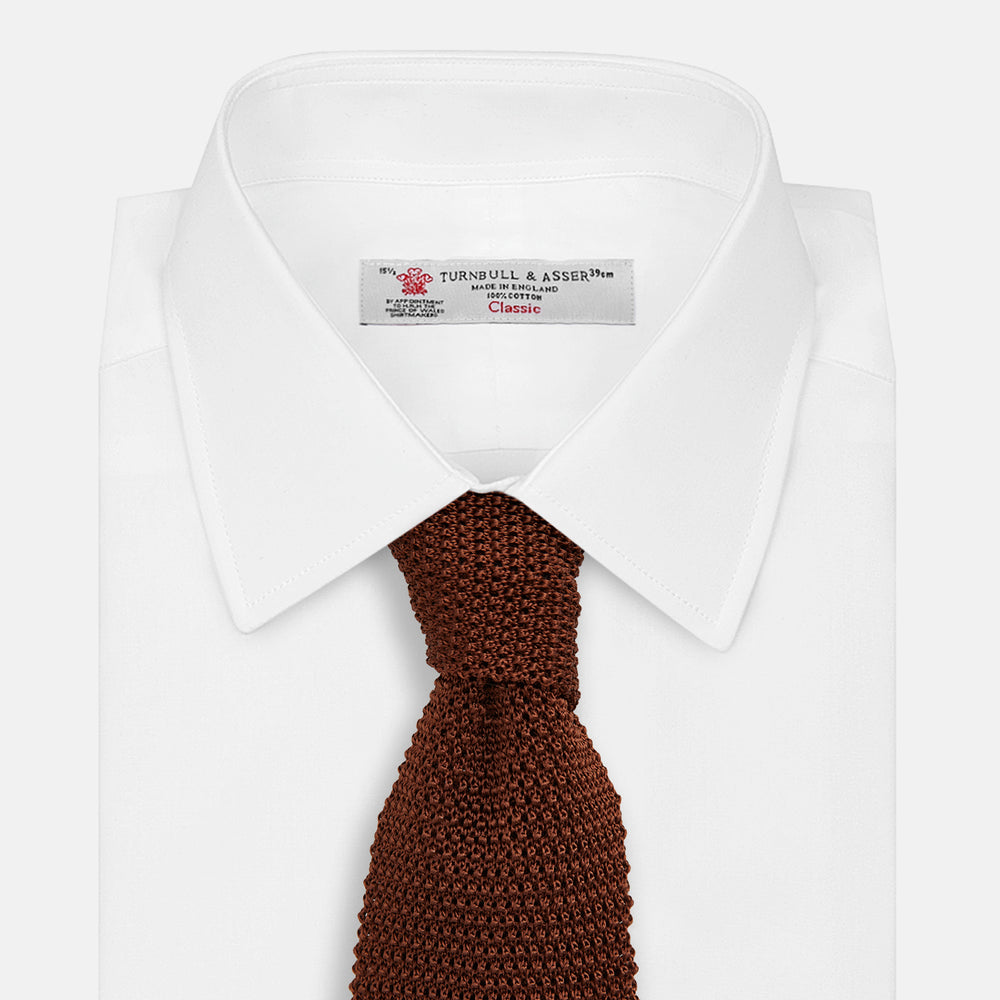 The Turnbull & Asser KNITTED BROWN SILK PLAIN TIE—a stylish, textured accessory—appears rolled up on a white background, perfect for elevating smart outfits.