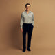 A man stands against a beige background wearing the Turnbull & Asser Cloud Blue Cashmerello Holiday Fit Fellows Shirt, styled with dark trousers, a black belt, and black shoes, looking directly at the camera with a neutral expression.