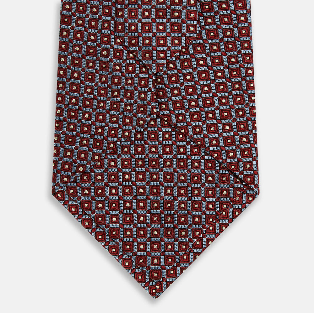 The Turnbull & Asser Burgundy Diamond Silk Tie features a red silk background with a repeating geometric diamond pattern of blue and white squares, exemplifying British craftsmanship.