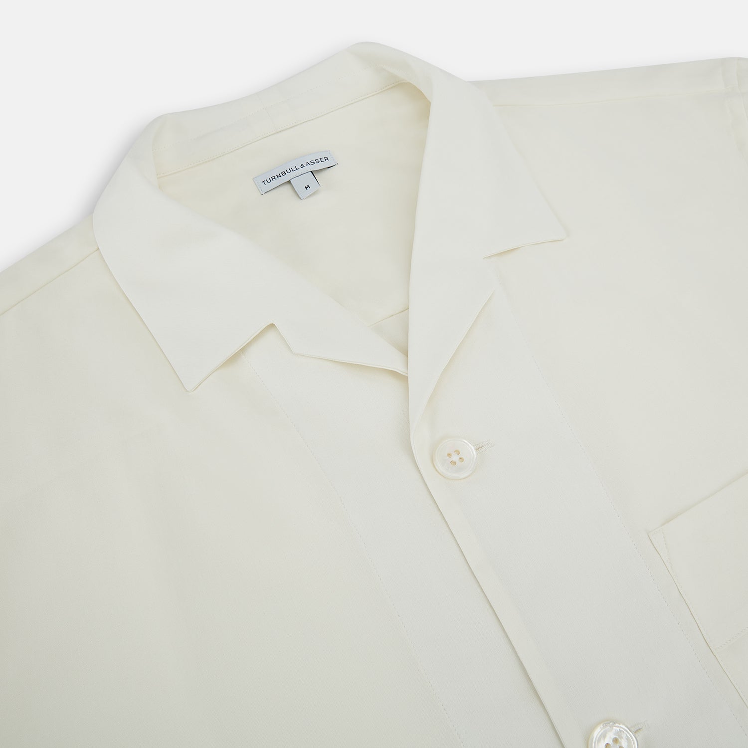 View 2 of product The Turnbull & Asser Cream Silk Pyjama Set, shown laid flat on a white background, features a long-sleeve button-up top with a chest pocket and matching pants with an elastic drawstring waist—ideal for comfortable loungewear.