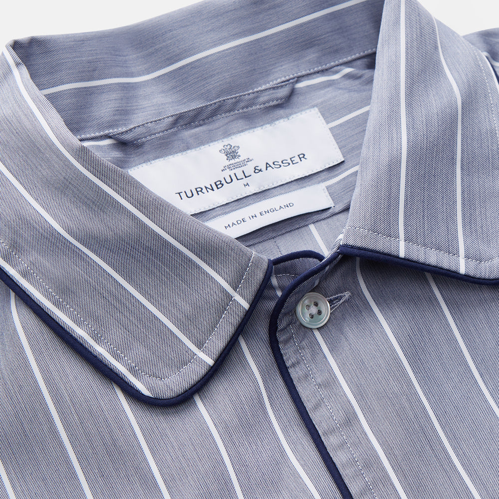 The Turnbull & Asser Pale Blue and White Pinstripe Cotton Blend Sussex Nightshirt pairs classic style with comfort, featuring long sleeves, a collar, front buttons, chest pocket, and curved hemline—perfect for luxury sleepwear.