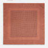 View 4 of product The Turnbull & Asser Blush Dot Silk Pocket Square features a rust hue with black polka dots, a bordered design, and hand-rolled edges, shown folded against a white background.