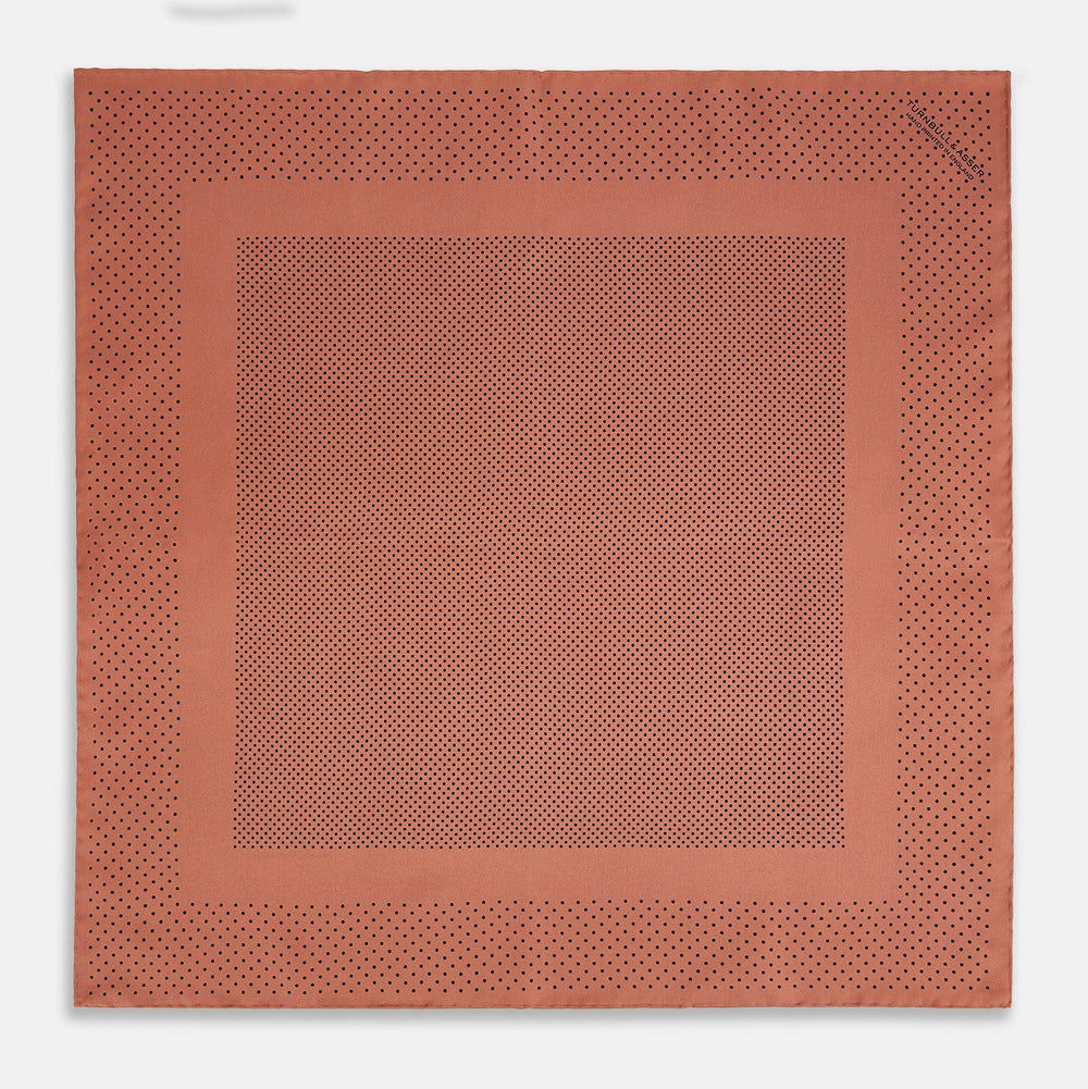 The Turnbull & Asser Blush Dot Silk Pocket Square features a rust hue with black polka dots, a bordered design, and hand-rolled edges, shown folded against a white background.