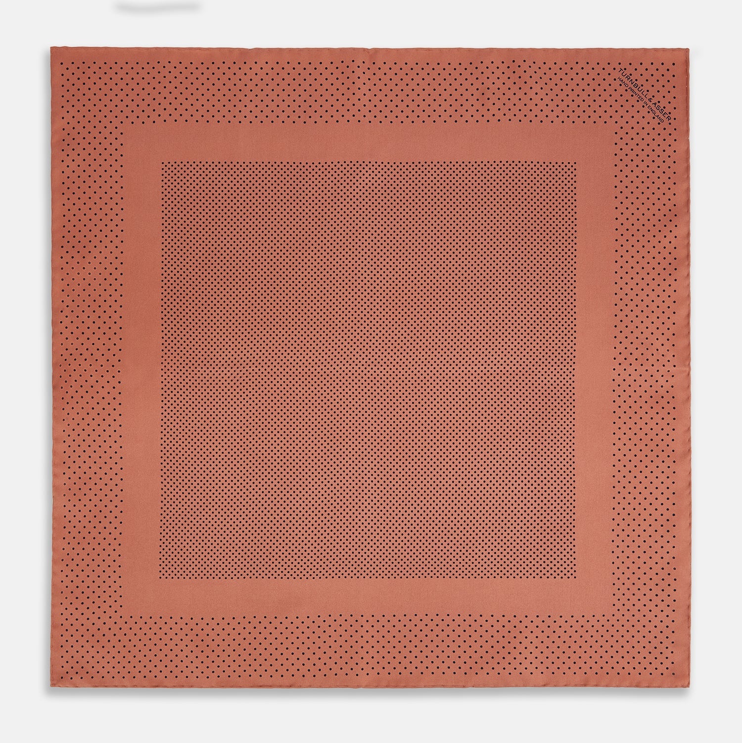 View 4 of product The Turnbull & Asser Blush Dot Silk Pocket Square features a rust hue with black polka dots, a bordered design, and hand-rolled edges, shown folded against a white background.