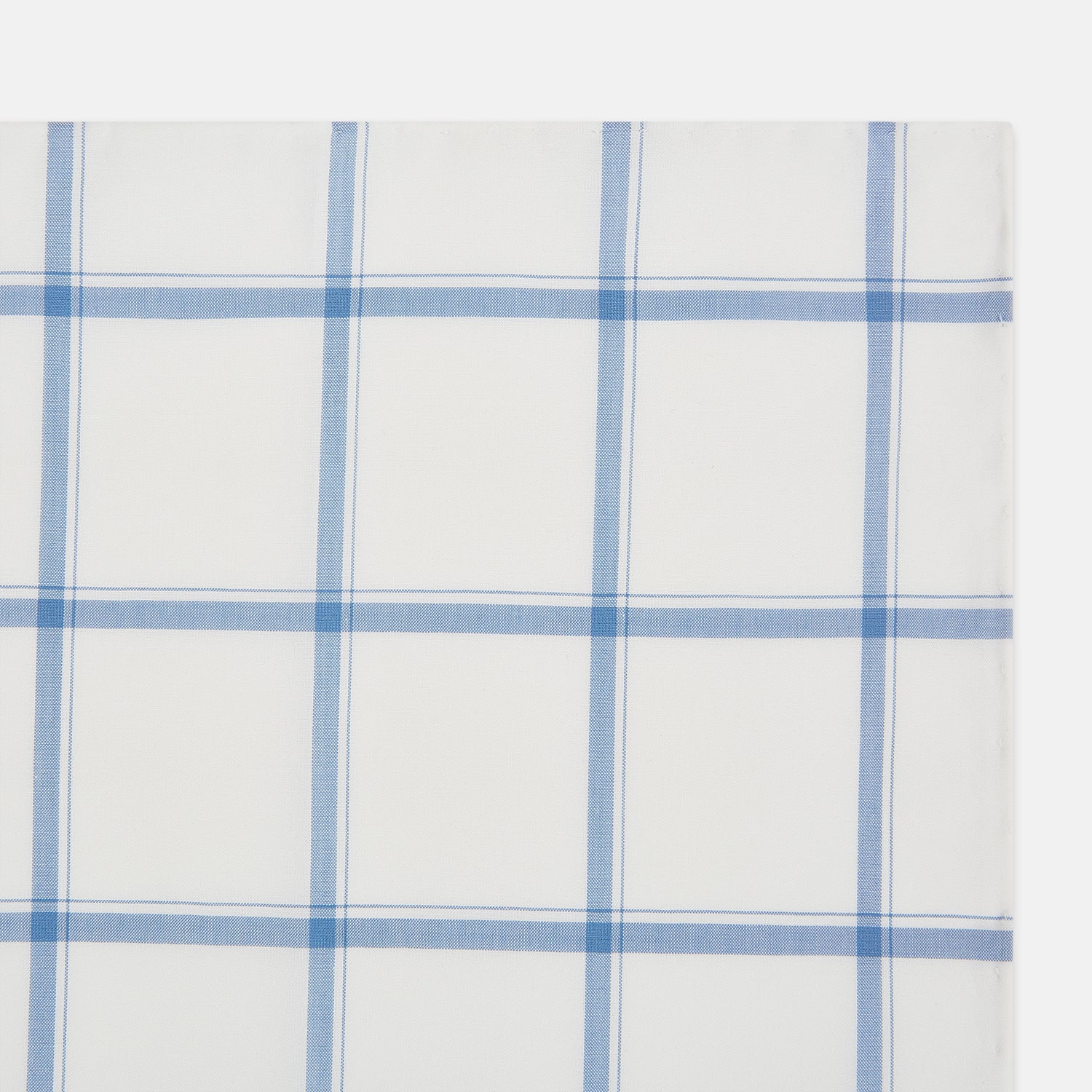 View 3 of product The Turnbull & Asser Colony Blue Grid Check Hand-Rolled Handkerchief features a white base with intersecting light and dark blue plaid lines forming squares, shown folded on a plain white background.