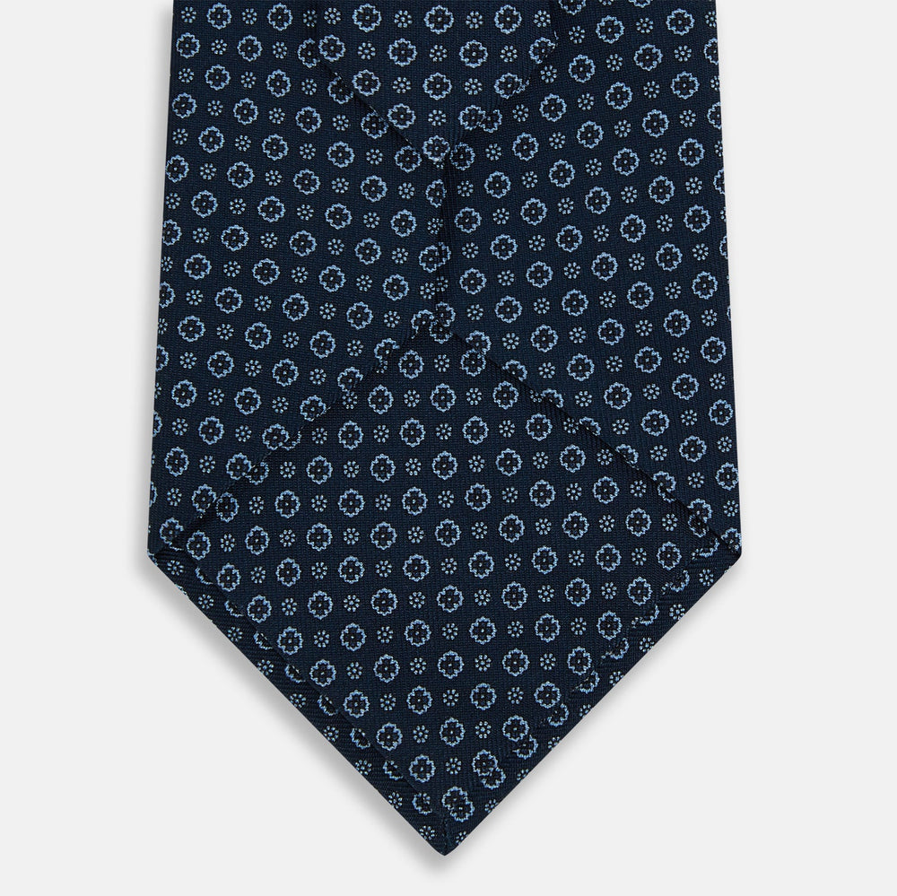 The Turnbull & Asser Navy Floral Silk Tie is crafted from fine English silk, featuring a repeating pattern of small white circular floral motifs, and is neatly rolled for display against a plain white background.