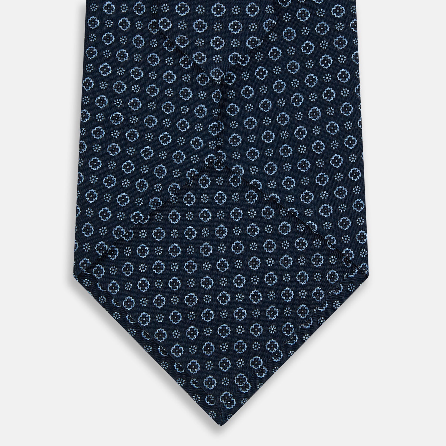 View 3 of product The Turnbull & Asser Navy Floral Silk Tie is crafted from fine English silk, featuring a repeating pattern of small white circular floral motifs, and is neatly rolled for display against a plain white background.