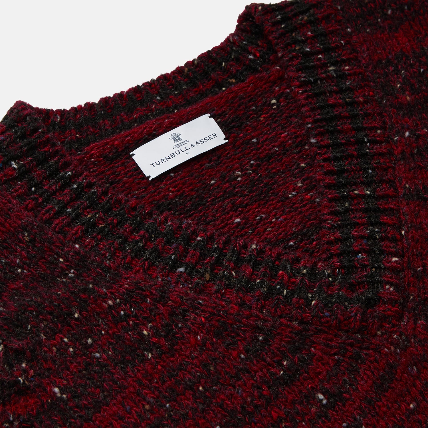 View 2 of product The Turnbull & Asser Russet Red Melange Wool Hafod Cricket Jumper features maroon and black speckles, a V-neck, long sleeves, and ribbed cuffs and hem, displayed flat on a white background.
