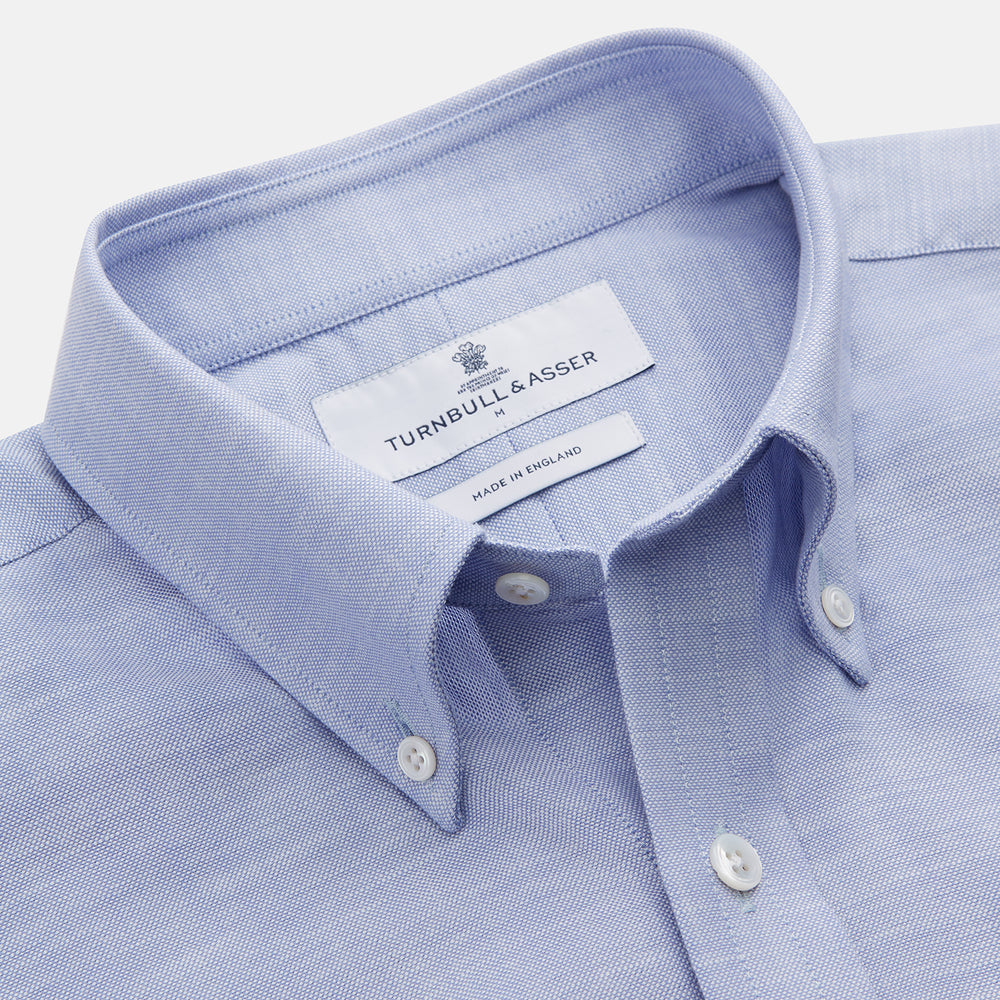 The Turnbull & Asser Pale Blue Weekend Fit Hayne Shirt features a Dorset collar, white buttons, and 1-button cuffs. This casual, long-sleeve button-down is displayed laid flat on a white background.