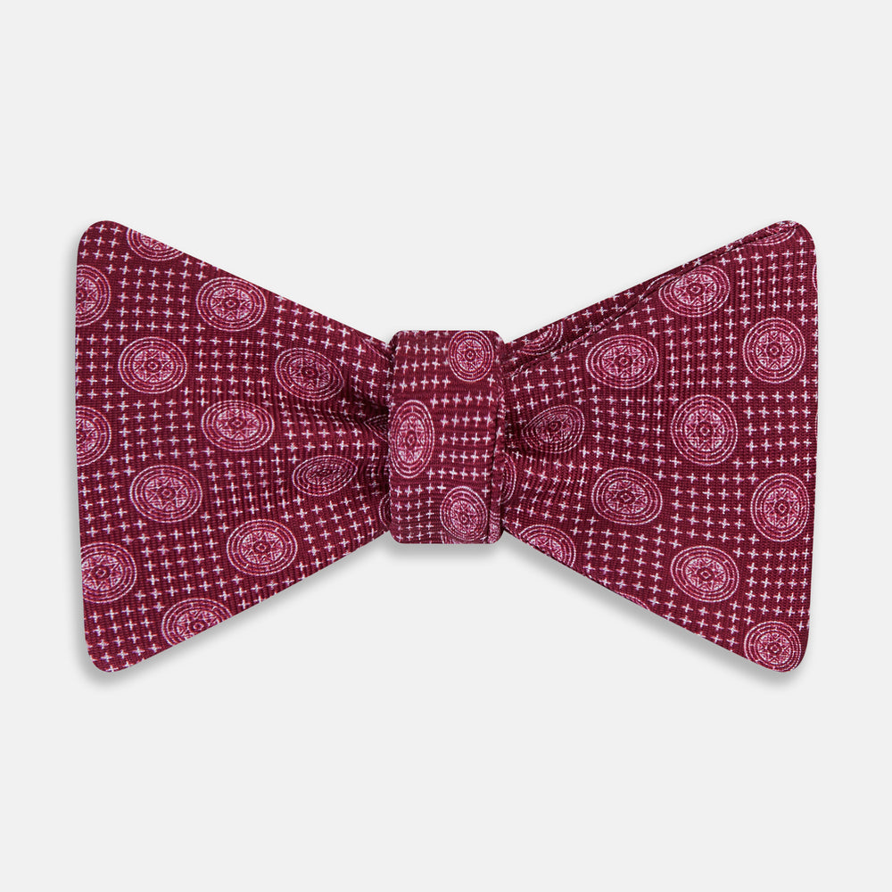 The Turnbull & Asser Burgundy Medallion Silk Bow Tie, featuring small white circles and crosshatch lines, is displayed on a plain white background—perfect for adding sophistication to smart attire.