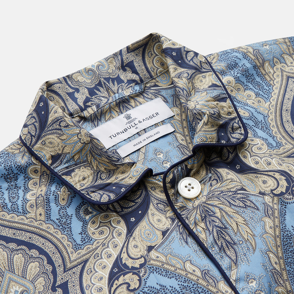 The Turnbull & Asser Pale Blue Baroque Silk-blend Hyde Pyjama Set features a long-sleeve button-up shirt and pants in a blue and beige paisley pattern, shown flat on a white background.