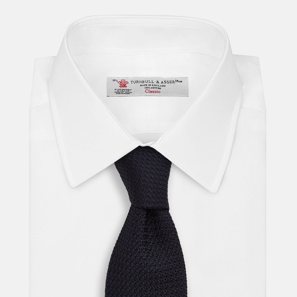 The GRENADINE NAVY TIE by Turnbull & Asser—a rolled, dark navy blue textured tie—serves as an essential accessory for smart outfits, shown against a plain white background.
