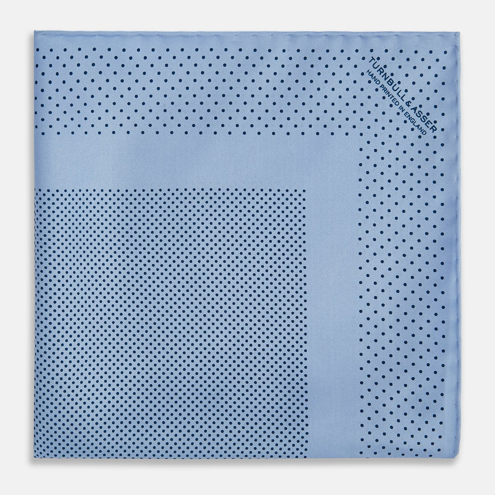 The Turnbull & Asser Pale Blue Dot Silk Pocket Square features pure silk in pale blue with a border and scattered small navy polka dots, neatly folded with one corner turned down.