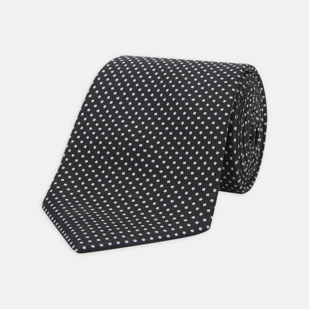 The Turnbull & Asser Black and White Small Spot Printed Silk Tie, shown rolled against a white background, features a subtle polka dot pattern—an ideal accessory for any office shirt.