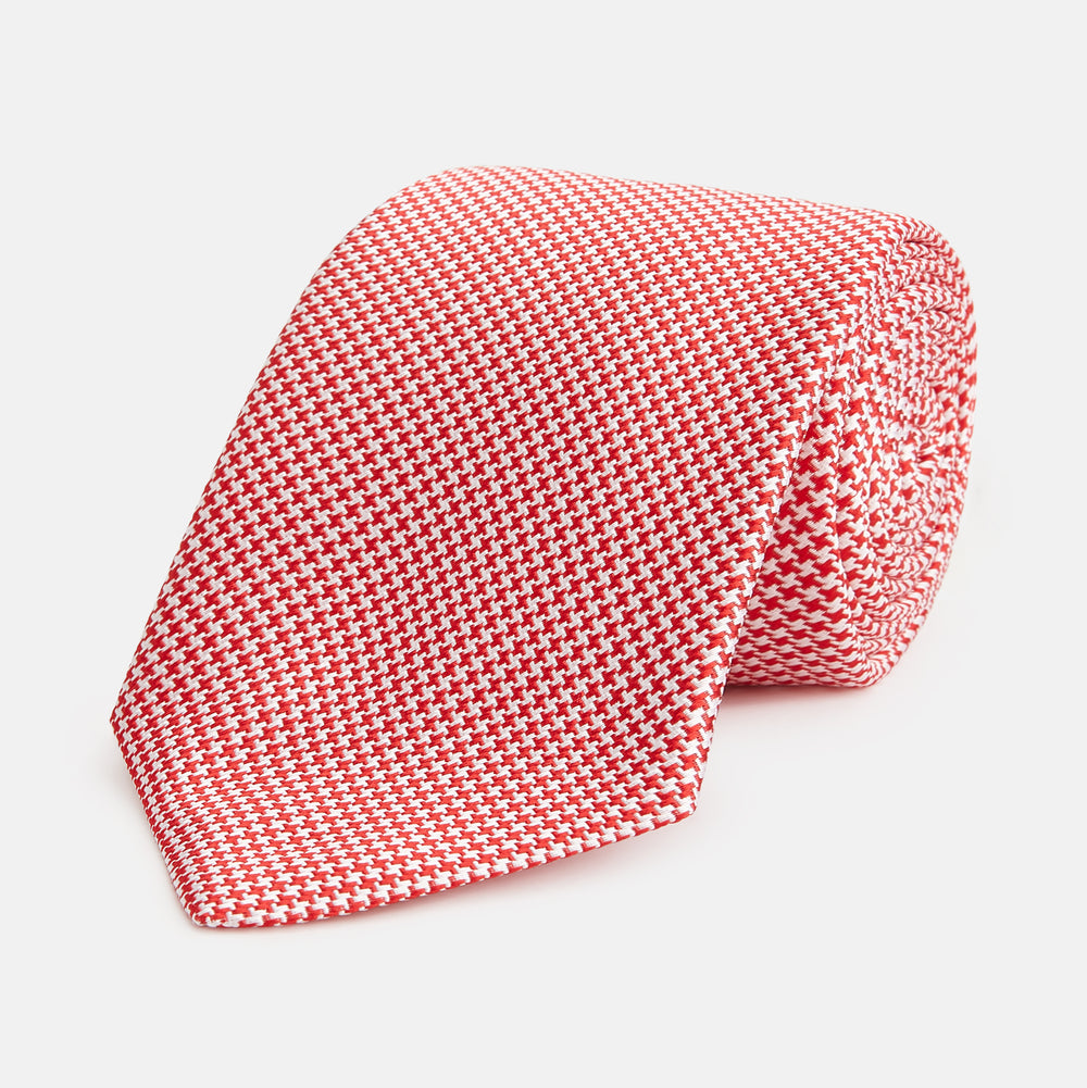 The Turnbull & Asser Red and White patterned silk tie, crafted from fine silk with a small geometric design, is elegantly rolled and displayed on a white background—a refined men’s accessory.
