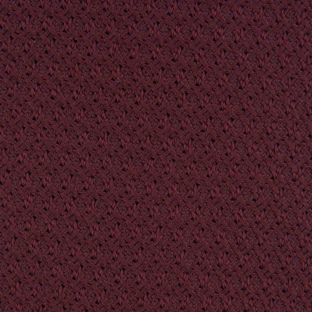The Turnbull & Asser Plain Woven Grenadine Silk Tie, shown rolled at one end on a white background, features a rich burgundy hue and textured pattern—an essential accessory for sophisticated looks.